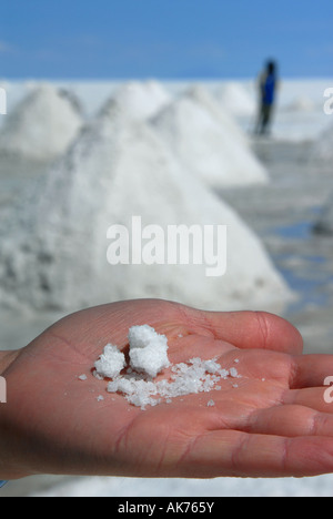 Una mano tiene il sale grezzo nella parte anteriore del sale gigante tumuli che sono impilati da locali ad asciugare sul Salar de Uyuni vicino a Uyuni, Bolivia Foto Stock