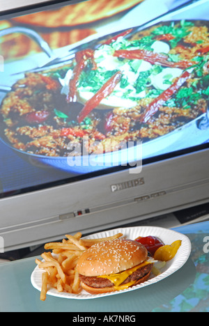 Concetto shot per mostrare malsana fast food TV cena davanti alla televisione programma di cucina che mostra un sano pasto fresco Foto Stock