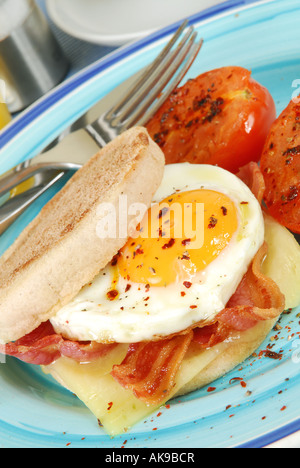 Colazione cotta di grigliate di back bacon rashers, il formaggio cheddar e uovo fritto su un tostato muffin inglese con pomodoro grigliate Foto Stock