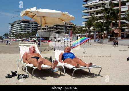 Coppia di anziani a prendere il sole insieme sotto l'ombrellone sulla spiaggia di Puerto Vallarta Messico Spiaggia Foto Stock