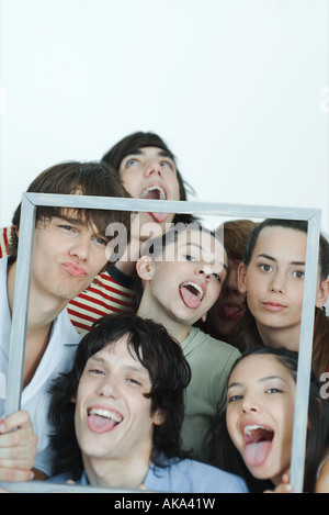 Un gruppo di giovani amici mantenendo la cornice immagine, rendendo le facce in telecamera, ritratto Foto Stock
