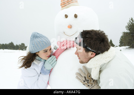 Coppia giovane guardando intorno pupazzo di neve a ciascun altro, sorridente, ritratto Foto Stock