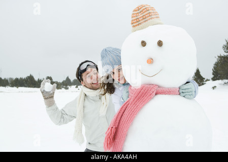 Abbracciando femmina pupazzo di neve e sorridente alla fotocamera, ragazzo in piedi dietro, mantenendo la palla di neve Foto Stock