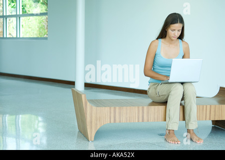 Ragazza seduta sul banco di lavoro, usando il computer portatile, guardando verso il basso Foto Stock