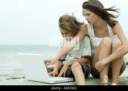 Teen girl e il fratello più piccolo utilizzando computer portatile insieme, ragazza rivolto oltre il ragazzo in spalla Foto Stock