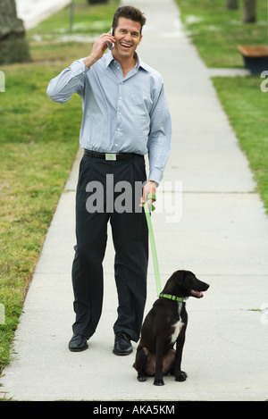 Uomo che cammina cane sul marciapiede, tramite telefono cellulare Foto Stock