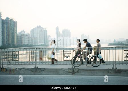 La Cina, nella provincia di Guangdong, Guangzhou, ciclisti e pedoni che attraversano il ponte, grattacieli di distanza Foto Stock