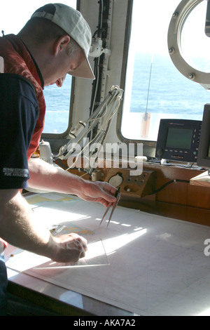 Responsabile della navigazione la tracciatura di un corso presso il banco di navigazione sul ponte di una nave. Foto Stock