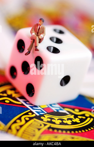 Piccola figura maschile in business suit seduti sui dadi e carte da gioco Foto Stock