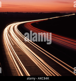 Il tramonto oltre i sentieri leggeri del veicolo, autostrada a tre corsie a doppia carreggiata sulla strada del Regno Unito al tramonto, capovolta per mostrare la guida su strade a sinistra, ad esempio la Francia Foto Stock