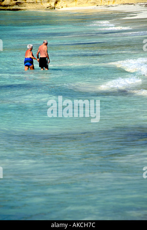 Una coppia di anziani camminare mano nella mano attraverso il surf in Antigua nei Caraibi. Foto Stock