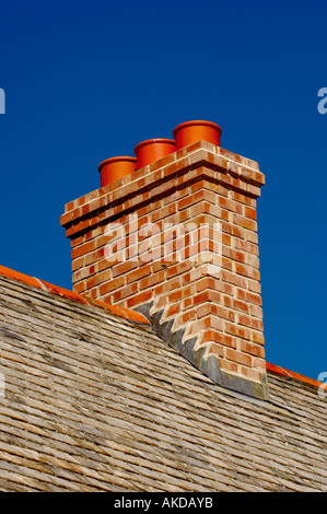 Camino in mattoni con vasi di terracotta in cima a un tradizionale tetto di ardesia della Cornovaglia, visto contro un cielo blu Foto Stock