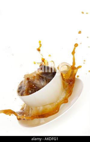 Il tè fuoriesce da una tazza bianca nel piattino mentre il latte viene versato. Tempesta in un teacup. Foto Stock