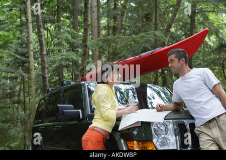 Coppia con mappa sul cofano auto in foresta Foto Stock