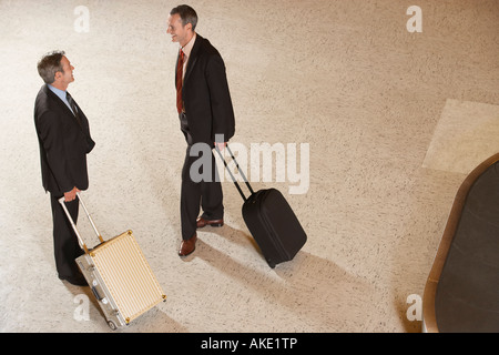 Due uomini di affari in piedi con le valigie dal carosello bagagli in aeroporto Foto Stock