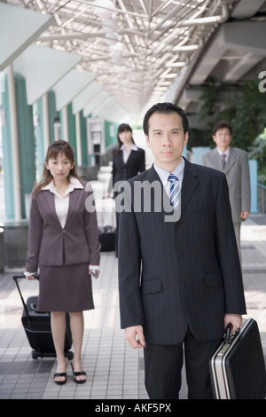 Imprenditore e a piedi tenendo la sua valigia con tre dirigenti aziendali in background Foto Stock