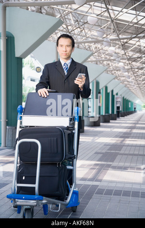 Imprenditore utilizzando un PC palmtop e spingendo un carrello portabagagli Foto Stock
