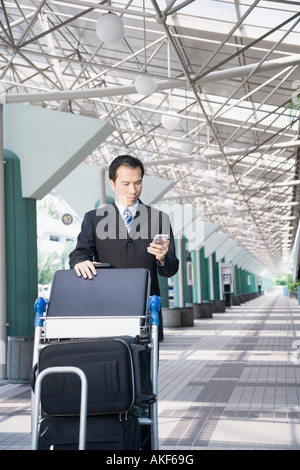 Imprenditore utilizzando un PC palmtop e spingendo un carrello portabagagli Foto Stock