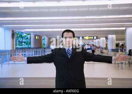 Ritratto di un imprenditore che si trova in piedi in una sala di attesa di un aeroporto con braccia aperte Foto Stock