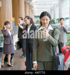 Imprenditrice guardando un telefono cellulare in un aeroporto Foto Stock