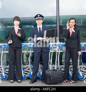 Ritratto di un pilota in possesso di un computer portatile e in piedi con due equipaggi di cabina in un aeroporto Foto Stock