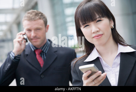 Close-up di una imprenditrice tenendo un assistente di dati personale con un imprenditore a parlare su un telefono mobile dietro di lei Foto Stock