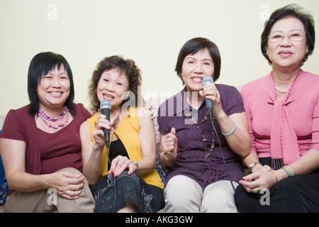 Tre le donne anziane e una donna matura di cantare davanti a microfoni Foto Stock