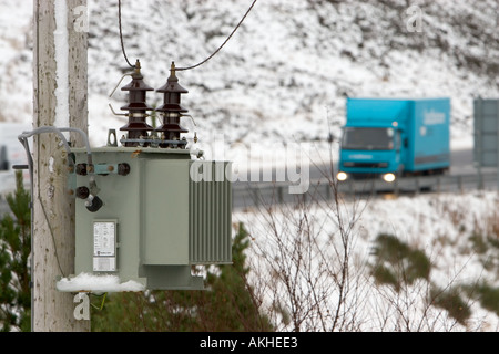 Trasformatore di distribuzione elettrica montato su palo nelle Highlands scozzesi con strada di montagna e camion blu sfocato sullo sfondo in scozia uk Foto Stock