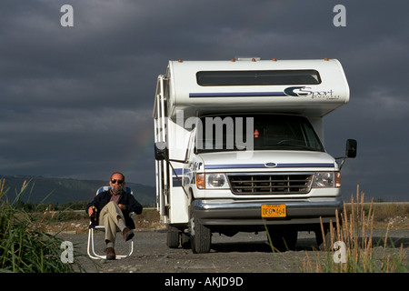 Uomo di bere birra e seduto nella sedia spiaggia di camper RV guardando il tramonto Homer Spit Alaska USA Foto Stock