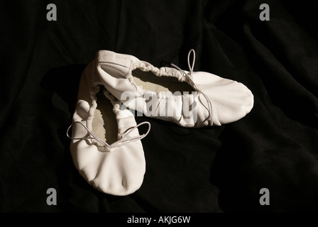 Un paio di scarpe da balletto in pelle bianca su sfondo nero, pantofole da ballo classiche in tonalità seppia Foto Stock