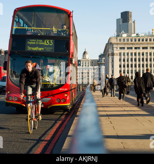 Red double decker Londra Trasporto bus e bicicletta ciclista attraversando ponte inizio mattina di sole Foto Stock