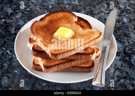 STACK DI quattro fette di pane tostato con il pezzo di burro fuso sulla parte superiore della piastra bianca di coltello e piano in granito Foto Stock