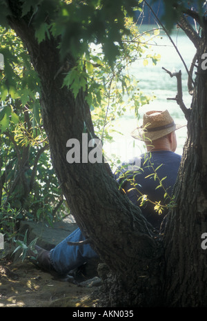 Uomo seduto sotto agli alberi dal lago Foto Stock