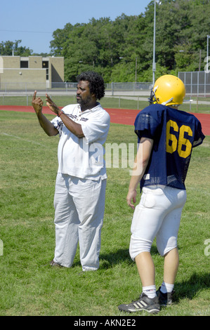 Alta Scuola Calcio azione Port Huron Michigan sordi JV giocatore di football legge la lingua dei segni data dal nero aiuto durante la pratica Foto Stock