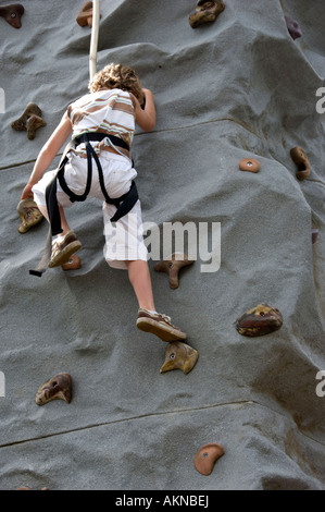 Ragazzo giovane salendo un modello di parete di roccia che indossa una imbracatura di sicurezza adottate in verticale con una copia dello spazio sul fondo Foto Stock