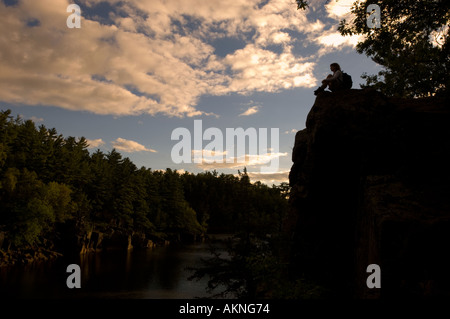 Donna escursionista seduti sulla rupe sopra St Croix fiume al tramonto Foto Stock