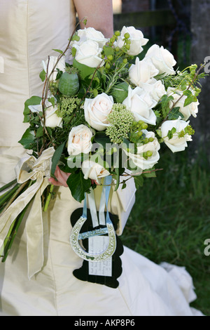 Ingrandimento dei dettagli di un appena sposato sposa il giorno delle nozze mentre tiene il suo bouquet di fiori e portafortuna ferro di cavallo dono Foto Stock