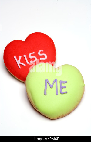 Due di colore rosso e verde satinato a forma di cuore i cookie o biscotti con Kiss Me scritta su di essi contro uno sfondo bianco Foto Stock