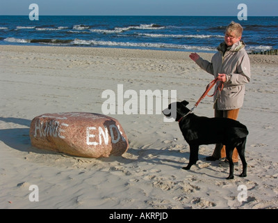 Donna con un cane nero sulla spiaggia di stare da un segno di confine su una pietra che mostra fine dell'area hanno consentito per cani Foto Stock