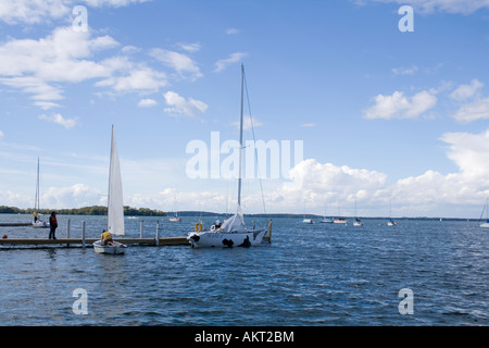 Barche a vela su un ampio corpo di acqua sotto un cielo blu con nuvole bianche a un dock. Foto Stock