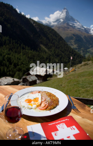 Röstinchen con uova fritte su una piastra con un bicchiere di vino rosso in un ristorante di montagna Findeln Matterhorn Zermatt Vallese Svizzera Foto Stock