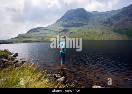 Giovane donna paddling in un Stickle Tarn con Harrison Stickle nella distanza. Parco Nazionale del Distretto dei Laghi, REGNO UNITO Foto Stock