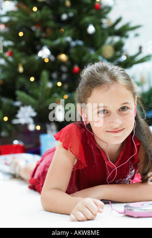 Bambina sdraiato da albero di natale l'ascolto di CD Player, ritratto Foto Stock