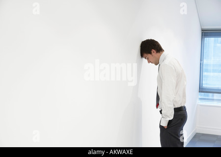 Imprenditore infelice in piedi con la testa contro il muro in ufficio vuoto Foto Stock