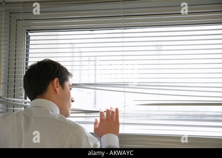 Imprenditore a guardare fuori dalla finestra di ufficio attraverso le veneziane, vicino, vista da dietro Foto Stock