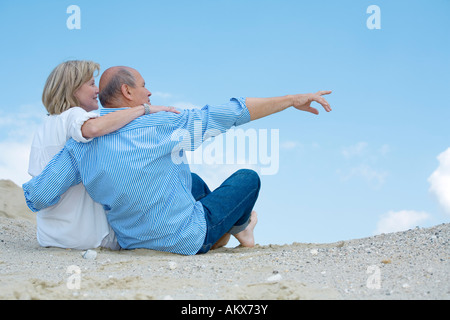 Coppia matura sittiing sulla spiaggia, un uomo indica Foto Stock