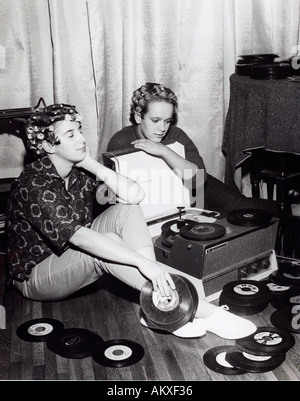 Due ragazze adolescenti in bigodini dreamily ascolto di 45 rpm registra su un annata record giocatore a casa nel 1950 s Foto Stock