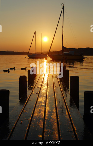 Tramonto con barca a vela e passerella sul lago Chiemsee, Chiemgau, Oberbayern, Bayern, Deutschland Foto Stock