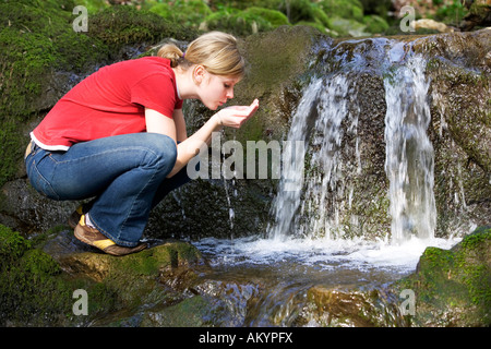 Giovane donna acqua potabile dal flusso, vista laterale Foto Stock