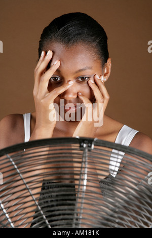 I giovani di carnagione scura donna nella parte anteriore del ventilatore, proteggendo la sua faccia con le mani Foto Stock